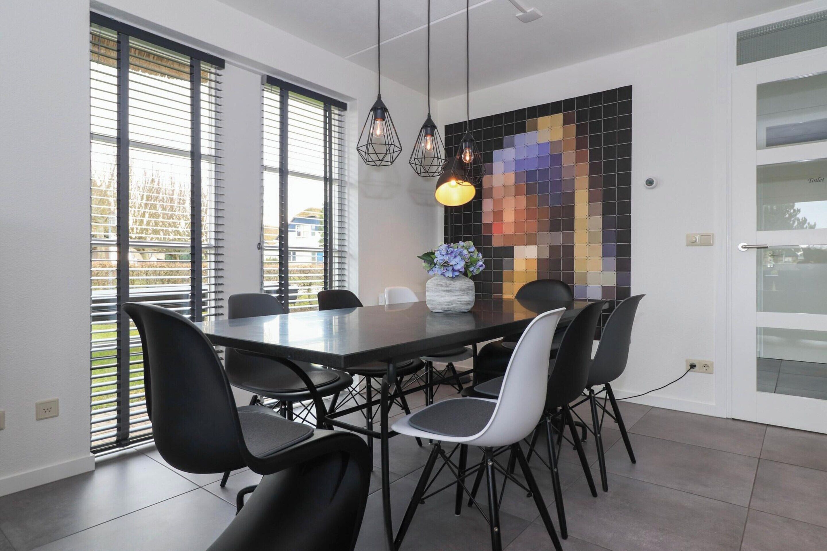 A modern dining area with a rectangular table, black chairs, pendant lights, and a decorative wall panel.