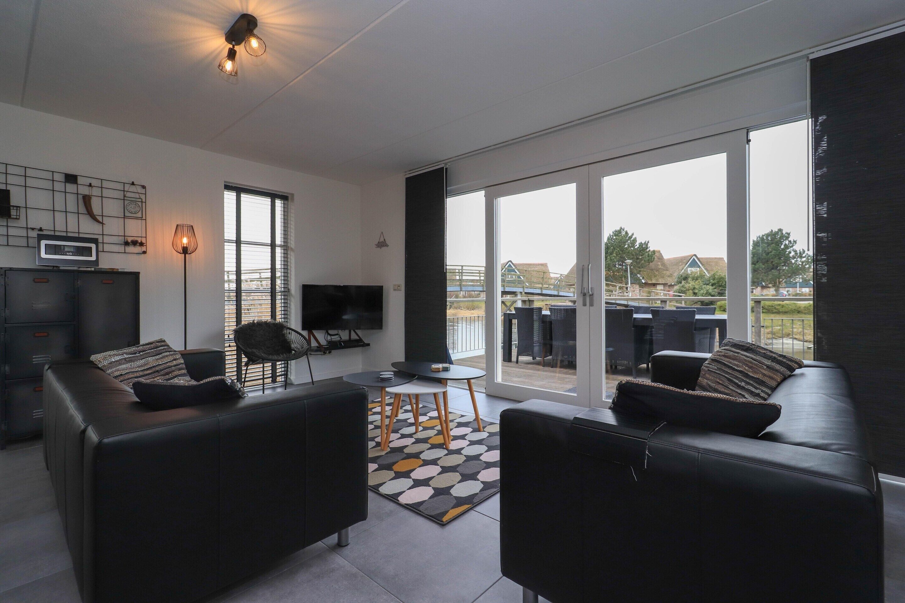 A modern living room with a flat-screen TV, two sofas, a coffee table, and a large sliding glass door leading to an outdoor patio.