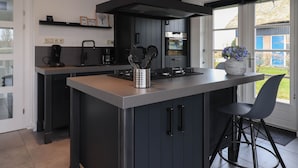 A modern kitchen with dark cabinetry, a central island, and a large window providing a view of the outdoors.