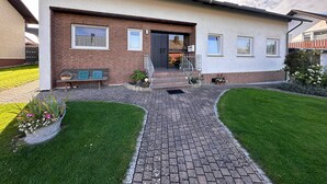 Une maison moderne à deux étages, dotée d’une façade en briques, de grandes fenêtres et d’une allée pavée menant à la porte d’entrée.