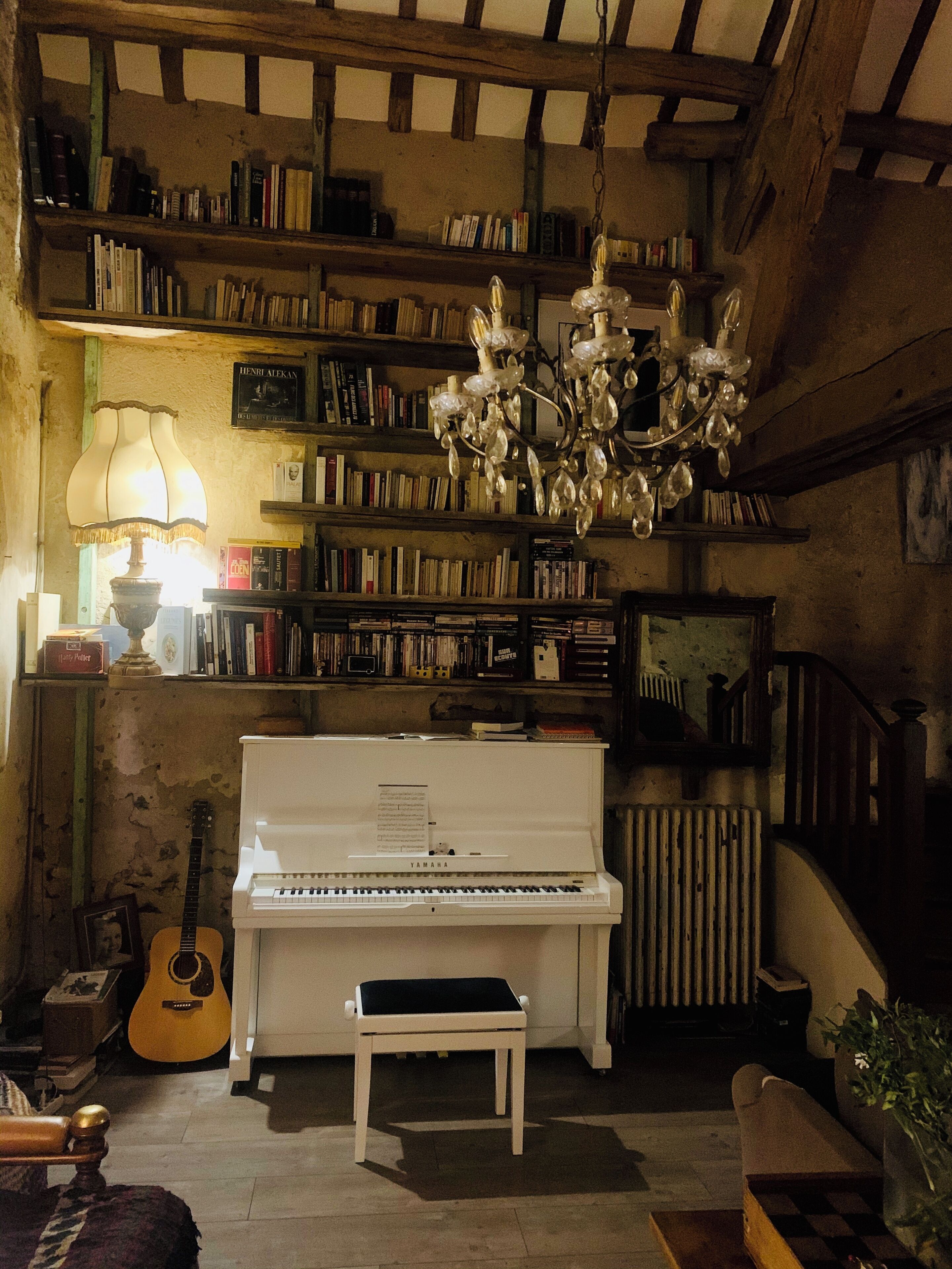 A cozy room with a piano, bookshelves, a chandelier, and a guitar.