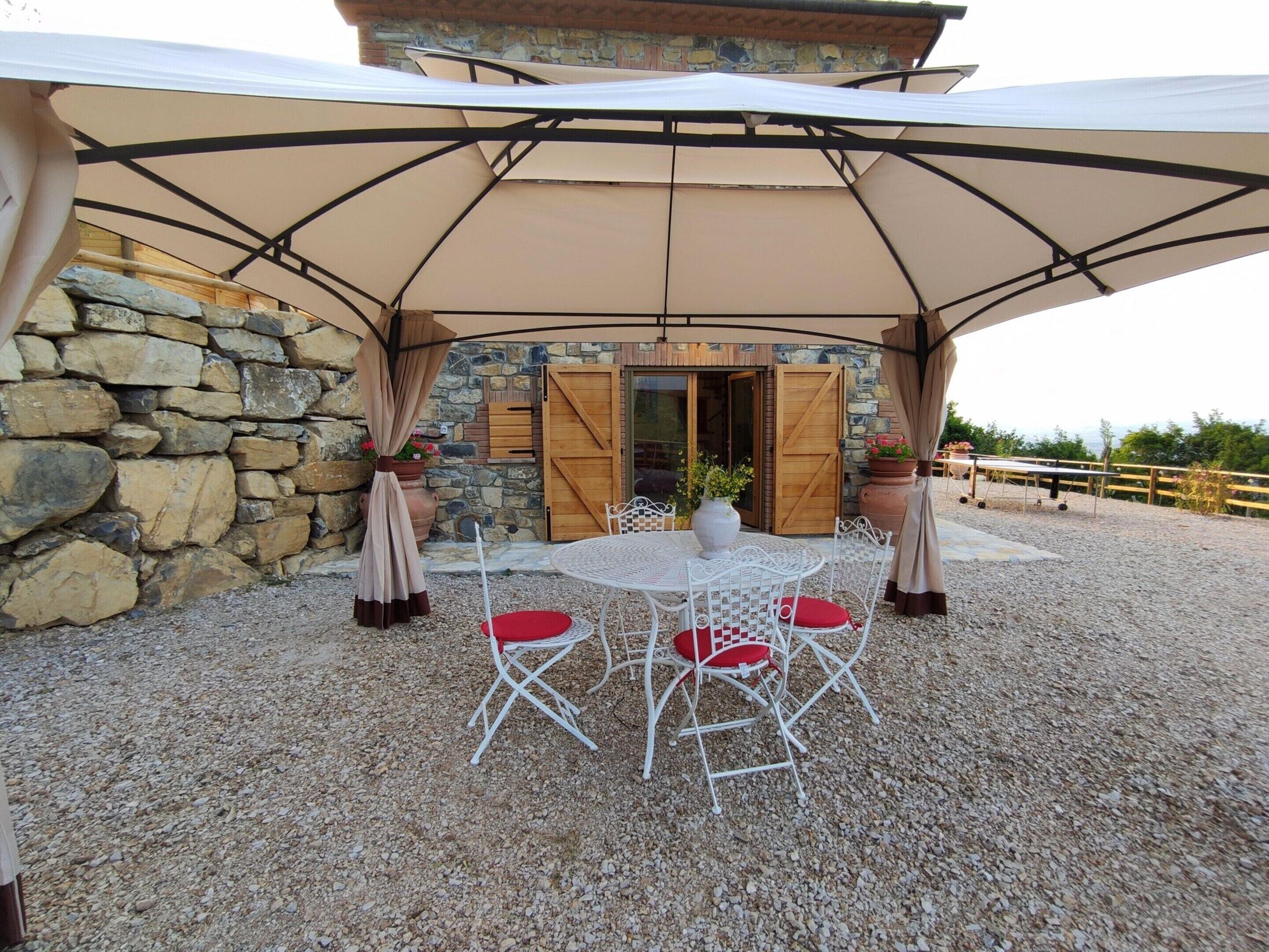 An outdoor patio with a round table and four chairs, a stone wall, and a wooden door.