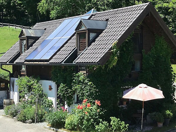A house with a sloped roof, solar panels, and a garden with flowers and plants. - Bergwiesen - Studio House (Traunstein)