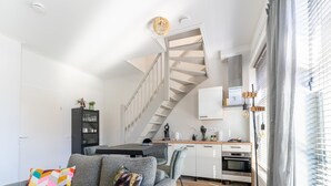 A modern living room with a grey sofa, a colorful pillow, a black cabinet, and a staircase leading to a kitchen area. - Modern Apartments in the Heart of Sneek (Sneek)