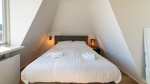 A bedroom with a sloped ceiling, a bed with white linens, two bedside lamps, and a window. - Modern Apartments in the Heart of Sneek (Sneek)
