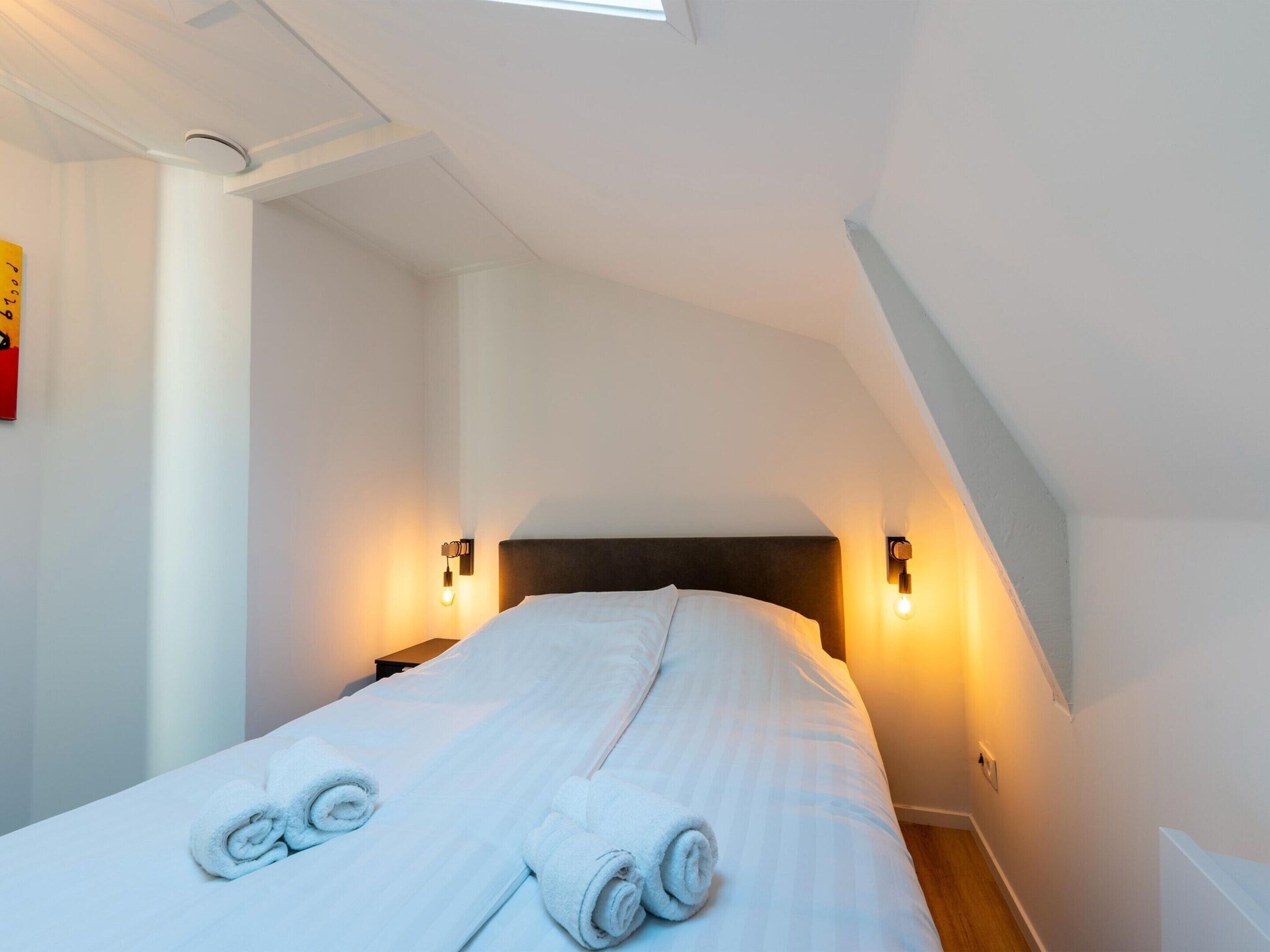 A hotel room with a large bed, two wall-mounted lights, and a skylight.