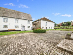 Um edifício de pedra tradicional com um pátio de calçada, um banco e um pequeno jardim.