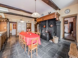 A rustic dining room with a large wooden table, chairs, and a fireplace.