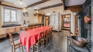 Un comedor espacioso con una larga mesa, sillas de madera y mantel rojo. Se observa una cocina con armarios de madera y estufa.