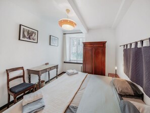 A bedroom with a bed, a wooden chair, a small table, a wardrobe, and a window with curtains.