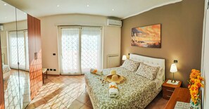 A bedroom with a bed, a nightstand, a lamp, a painting, and a view of the outdoors. - 3 Bedroom Villa in Fregene (Fregene)