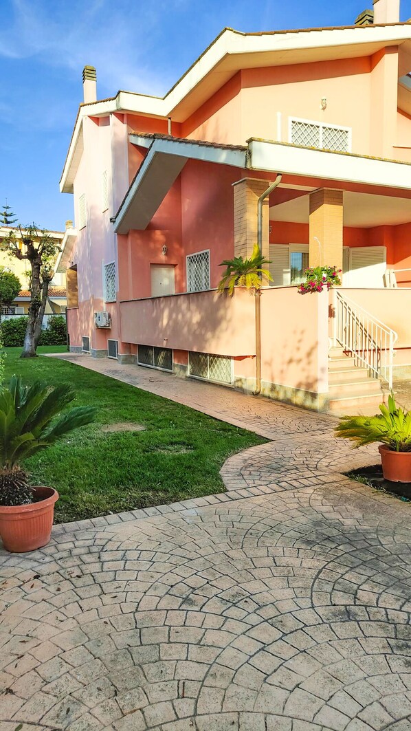A building with a paved walkway, a staircase, and potted plants. - 3 Bedroom Villa in Fregene (Fregene)