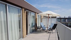 A balcony with two lounge chairs, a white umbrella, and a glass door leading to a room. - Apartment in Nieuwpoort With Beach Access (Nieuwpoort)