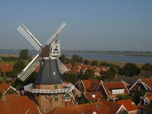 A traditional windmill with a black roof and white lattice structure, surrounded by red-roofed houses and a body of water in the background. - See.eck Timmel Modern Retreat (Grosefehn)