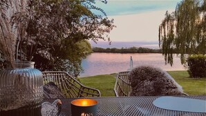 A table with a candle and a heart-shaped ornament, overlooking a lake with a chair and a vase nearby. - See.eck Timmel Modern Retreat (Grosefehn)