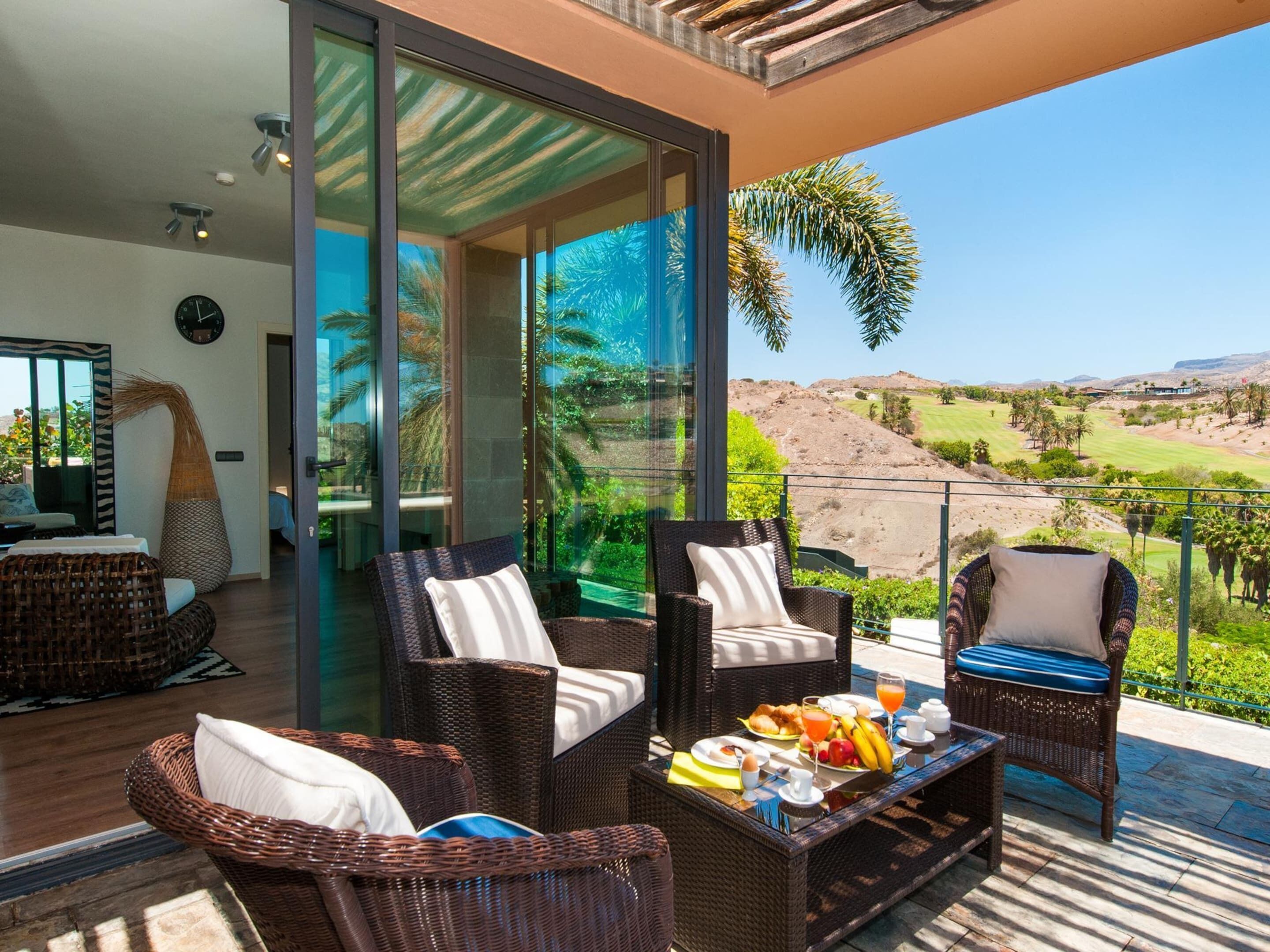 Un área de estar moderna al aire libre con mobiliario de mimbre y una mesa para el desayuno.