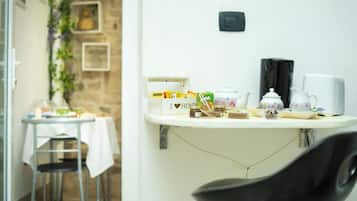 Une petite cuisine équipée d’un plan de travail blanc, d’une machine à café, d’une bouilloire et d’une boîte sur laquelle est écrit : « J’aime ma maison ».