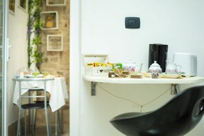 Une petite cuisine équipée d’un plan de travail blanc, d’une machine à café, d’une bouilloire et d’une boîte sur laquelle est écrit : « J’aime ma maison ».