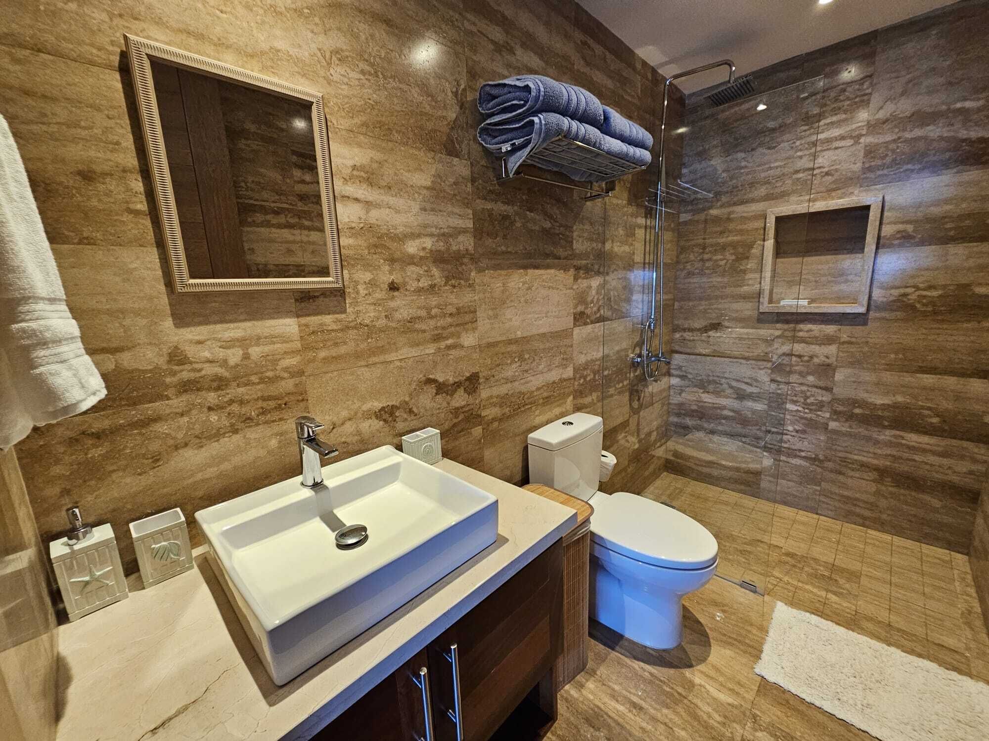 Une salle de bain moderne avec un grand miroir, un lavabo blanc, des toilettes et une douche à parois de verre.