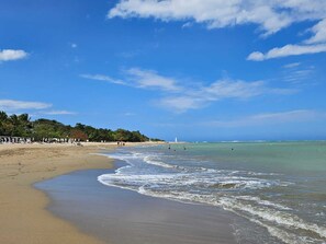 A beach with clear blue skies, calm waves, and a few people in the water. - Playa Dorada: Cozy family friendly beachfront 3 bedroom /3 bathroom apartment. (Puerto Plata)