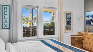 Un dormitorio con una cama grande, vistas a palmeras y montañas a través de la ventana, un aparador de madera y un letrero en la pared que dice "RELAX".
