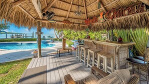 Una terraza de madera con techo de paja, una zona de bar y vistas a la piscina.