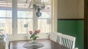 Une table à manger ornée d’un vase de fleurs, d’une lampe, et offrant une vue sur les arbres et un drapeau à l’extérieur.