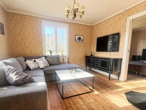 A living room with a sectional sofa, a glass coffee table, a black TV stand, and a window with a view of trees. - 7 Person Holiday Home in Forsheda (Forsheda)