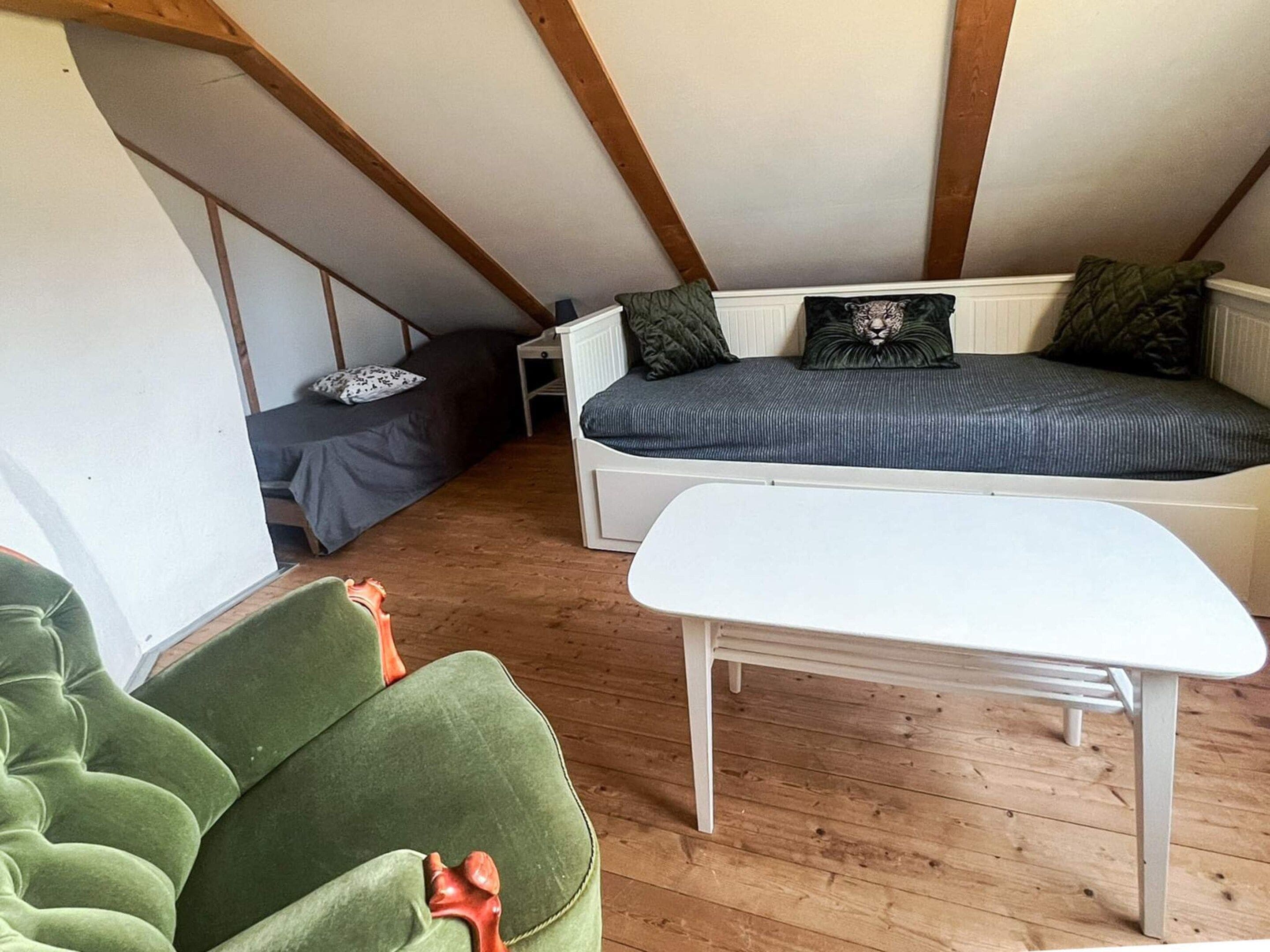 A loft bedroom with a sloped ceiling, a built-in bed, a white table, and a green armchair.