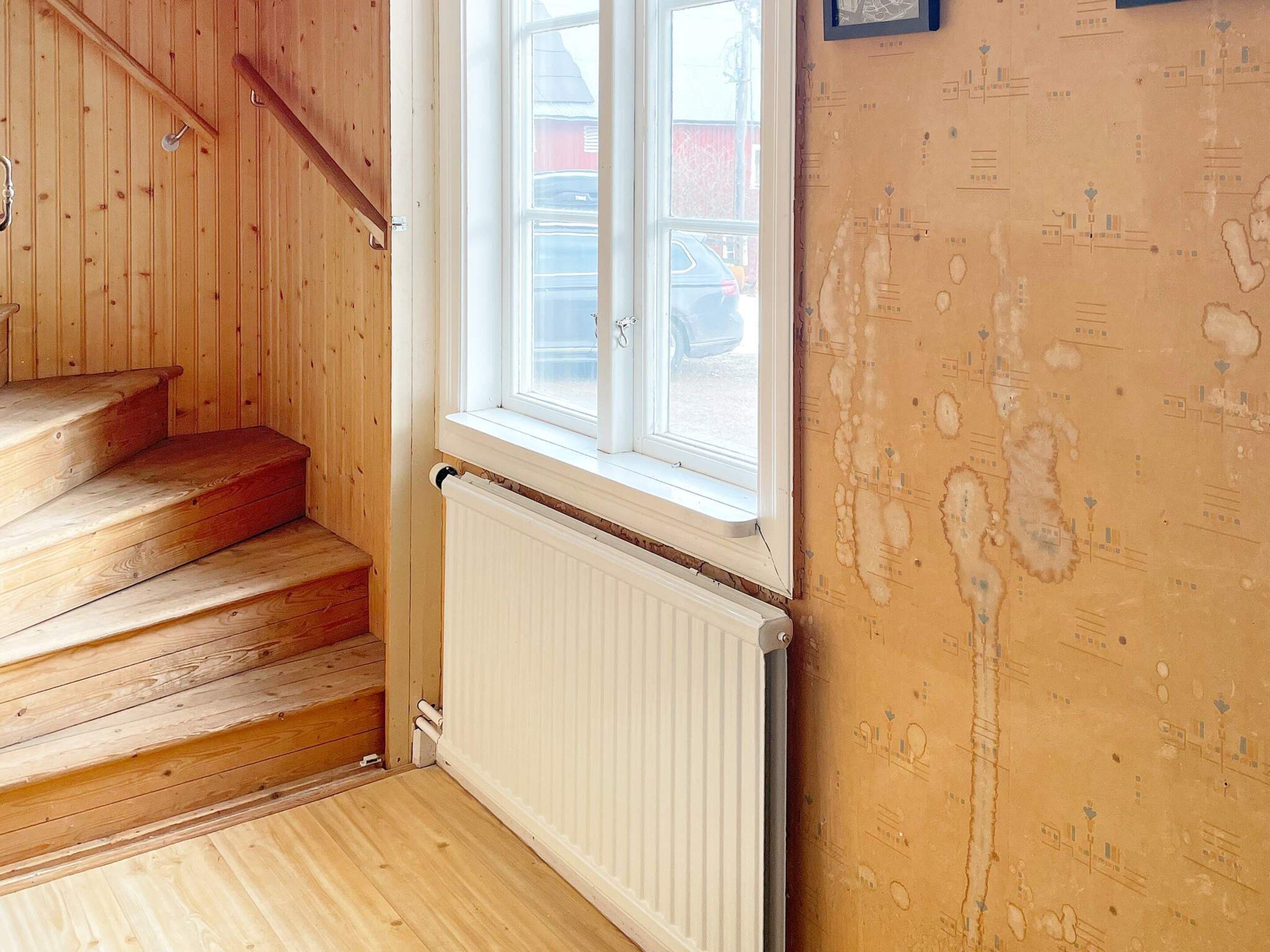 Un escalier en bois mène à une fenêtre d’où l’on peut voir une voiture à l’extérieur.