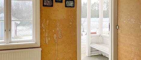A room with a yellow wall, a white door leading outside, and a window with a view of a snowy landscape.