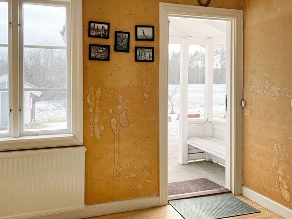 A room with a yellow wall, a white door leading outside, and a window with a view of a snowy landscape. - 7 Person Holiday Home in Forsheda (Forsheda)