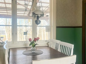 A dining area with a table, chairs, a vase with flowers, a hanging lamp, and a view of trees and a flag outside. - 7 Person Holiday Home in Forsheda (Forsheda)