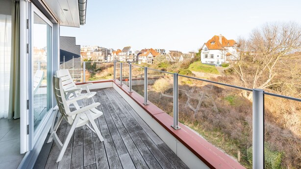 Ein Balkon mit weißen Stühlen, einer Holzterrasse und Blick auf Häuser im Hintergrund.