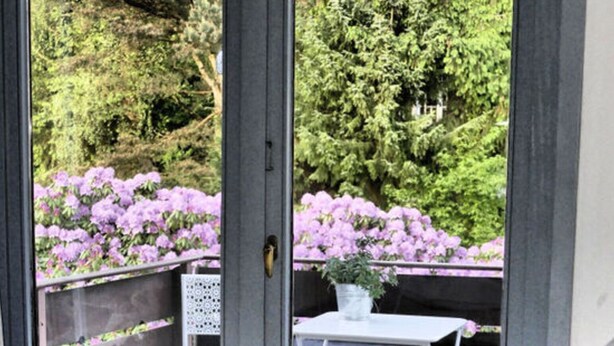 A bedroom with a bed, a small table with a chair, and a view of purple flowers through a window. - Holiday Apartment Green House (Aumuehle)