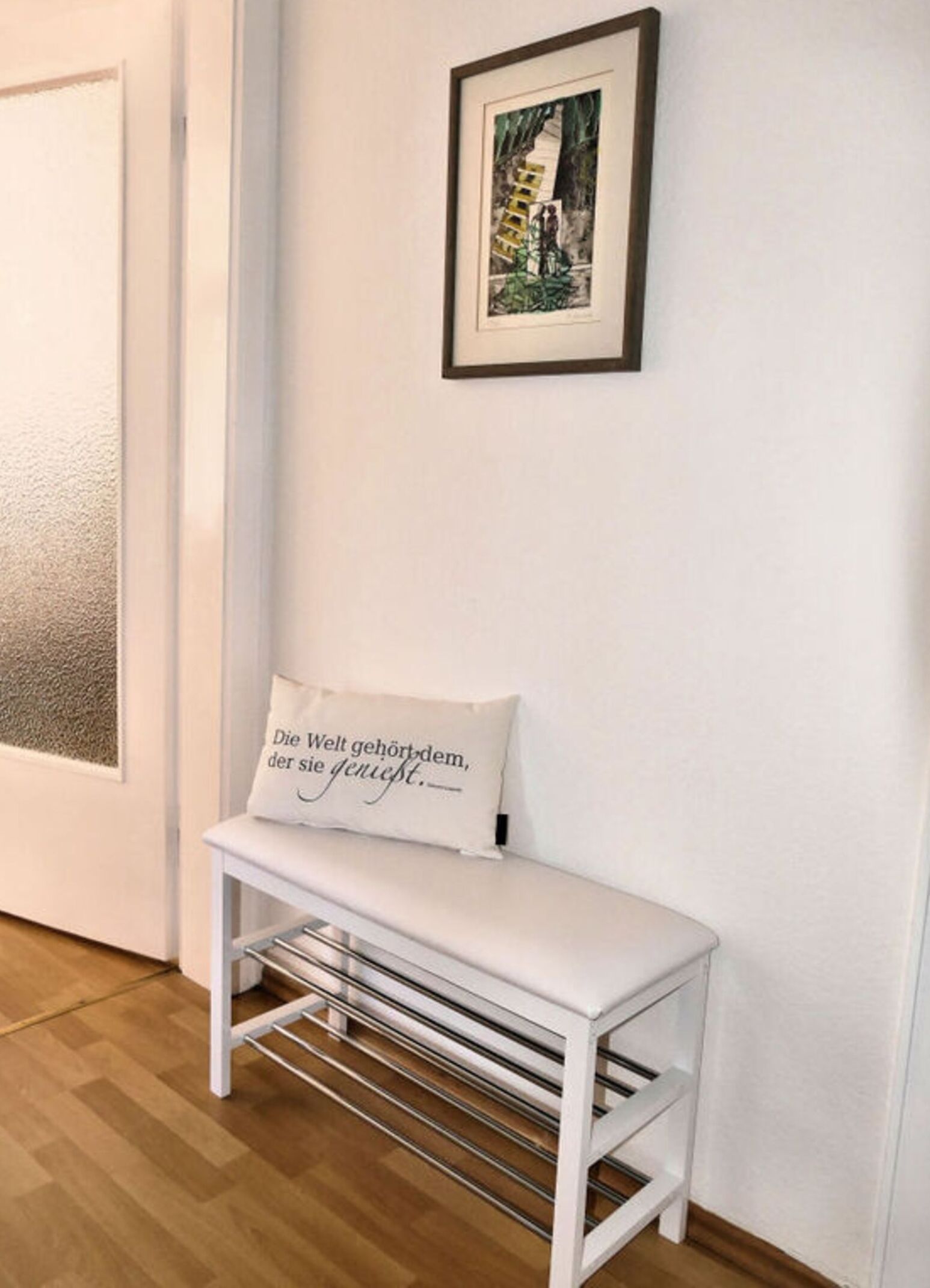 A white bench with a cushion in a room with wooden flooring and a white wall.