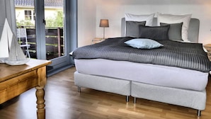 A bedroom with a large bed, a wooden nightstand, a lamp, and a view of the outside balcony. - Holiday Apartment Green House (Aumuehle)