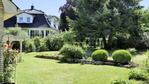 A house with a well-maintained garden, a stone wall, and a large tree. - Holiday Apartment Green House (Aumuehle)
