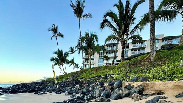 A beach with the word "Mahalo" written in the sand, palm trees, and a building in the background.