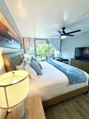 A bedroom with a large bed, a ceiling fan, a television, and a window with curtains.