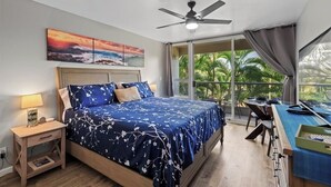 A bedroom with a bed, a desk, a chair, a ceiling fan, a nightstand, and a window with a view of palm trees.