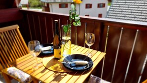 A wooden table set for two with a bottle of wine, a glass, and a small vase with a flower.