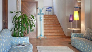 Ein Wohnzimmer mit Treppe, einem blauen Sofa, einer Topfpflanze und einer Lampe.