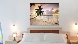 Ein Schlafzimmer mit einem Bett, zwei Nachttischen, einem Fernseher und einem Wandbild mit einer Strandansicht.