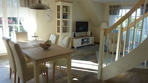 A spacious living room with a wooden dining table, comfortable chairs, a television, and a staircase leading to an upper level. - Beach & Good Comfortable Holiday Residence (Zingst)