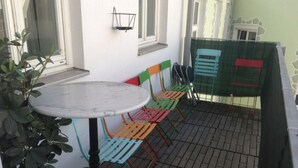Un espace patio avec une table ronde et des chaises colorées, une petite plante en pot et une fenêtre munie d’un grillage métallique.