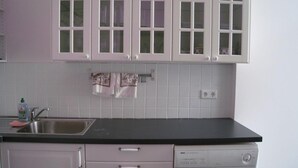 Une cuisine avec des meubles blancs, un plan de travail noir, un lave-linge et un évier.