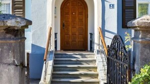 A building with a central arched entrance, a wooden door, and a staircase leading up to it. - In het Blauwe Huis - Zolderverdieping (Garmisch-Partenkirchen)