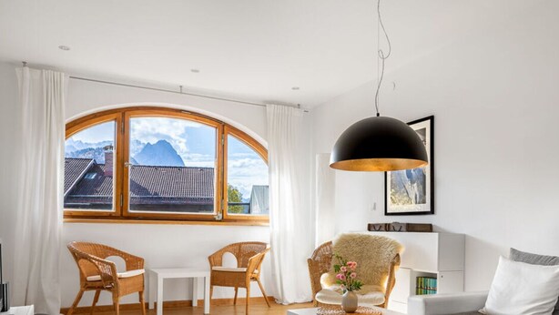 A modern living room with a large window, wicker furniture, a white sofa, and a black pendant light. - In het Blauwe Huis - Zolderverdieping (Garmisch-Partenkirchen)