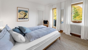 A bedroom with a bed, a window with curtains, a radiator, and a poster on the wall. - In het Blauwe Huis - Zolderverdieping (Garmisch-Partenkirchen)